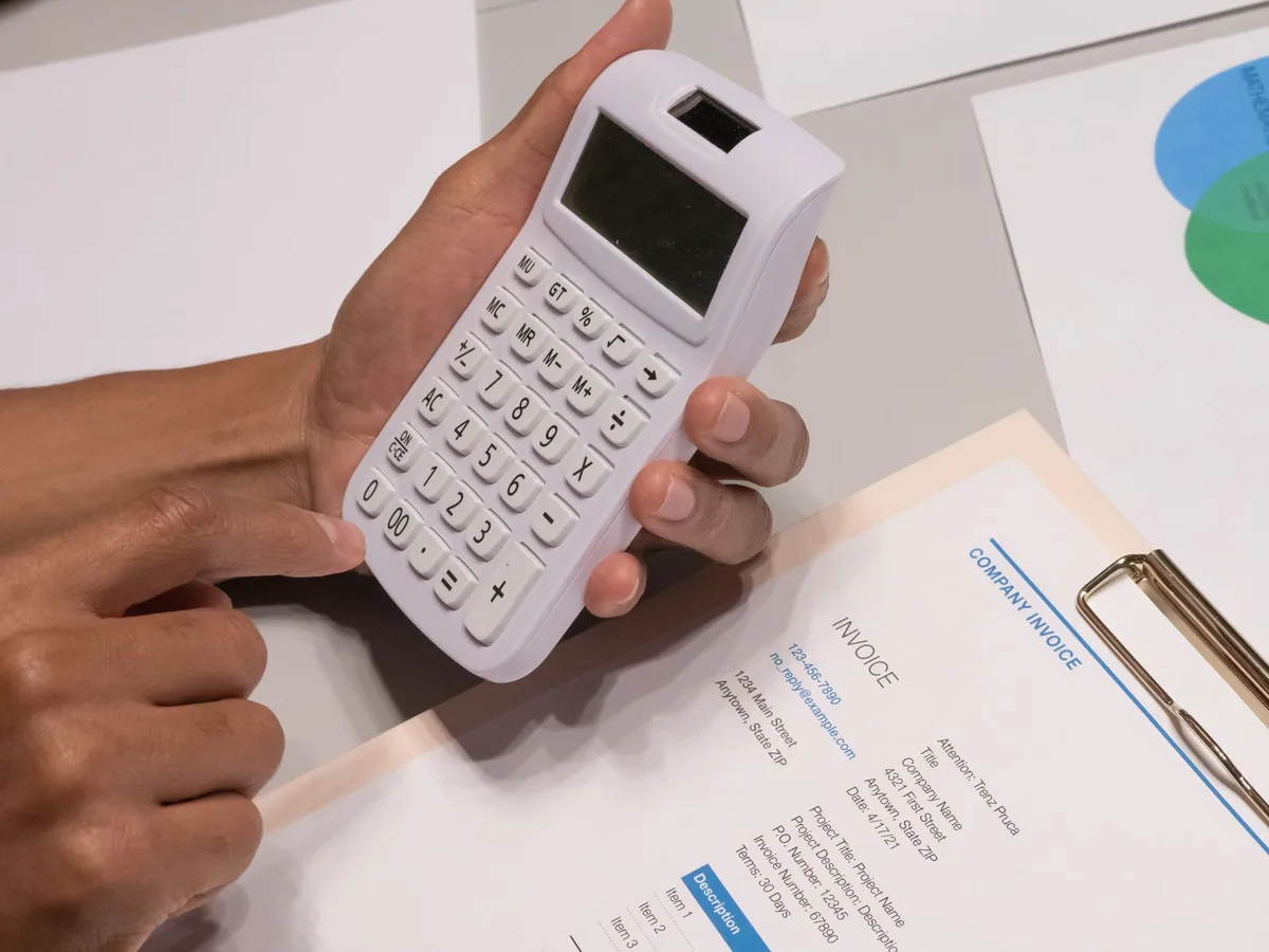 Close-up of hands using a calculator next to an invoice, working out a sale total